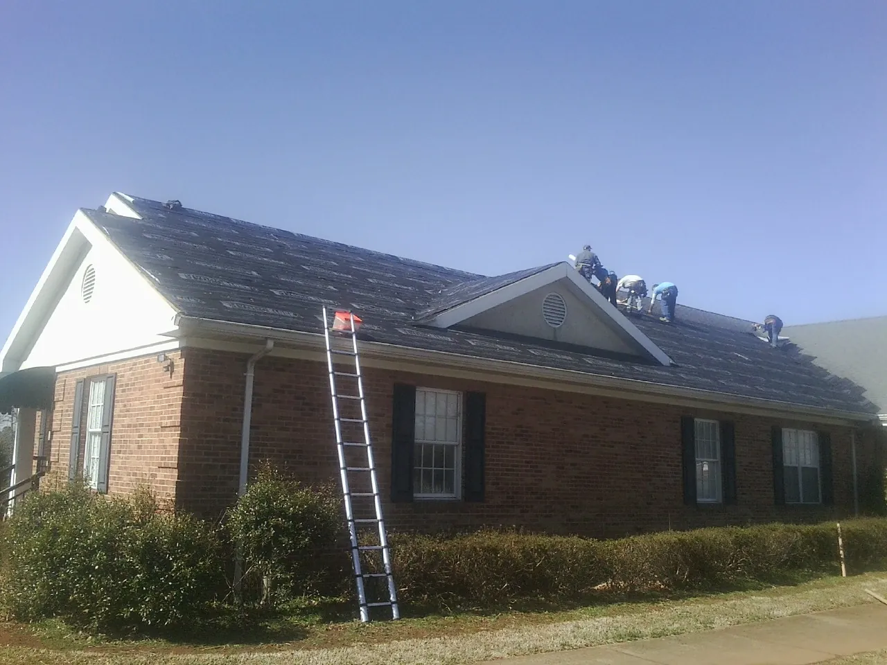 Crew tearing shingles off a brick ranch roof with a ladder set — Emergency Roof Repair work by our crew in Chester